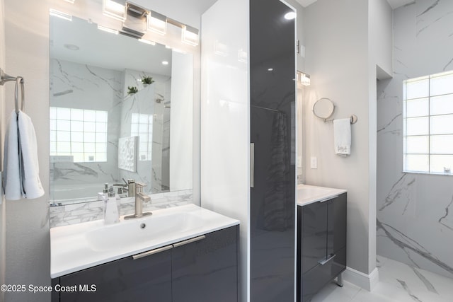 bathroom featuring marble finish floor, two vanities, a healthy amount of sunlight, and a sink