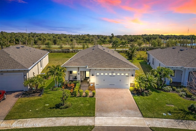 ranch-style home with stucco siding, decorative driveway, a yard, a shingled roof, and a garage