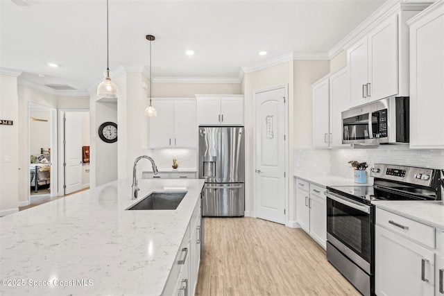 kitchen featuring crown molding, light wood-type flooring, appliances with stainless steel finishes, white cabinets, and a sink