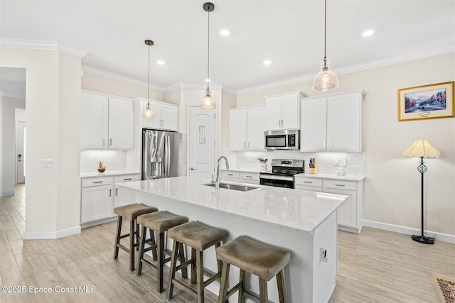 kitchen featuring a center island with sink, a sink, appliances with stainless steel finishes, a breakfast bar area, and crown molding