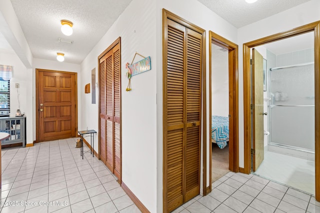 corridor with light tile patterned floors, baseboards, and a textured ceiling