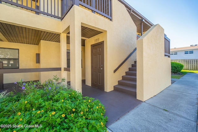 view of exterior entry featuring stucco siding, a balcony, and fence