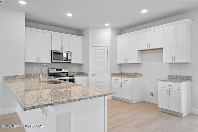 kitchen with light wood-type flooring, light stone counters, a peninsula, stainless steel appliances, and white cabinetry