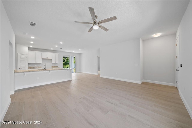 unfurnished living room with baseboards, light wood-style floors, visible vents, and ceiling fan