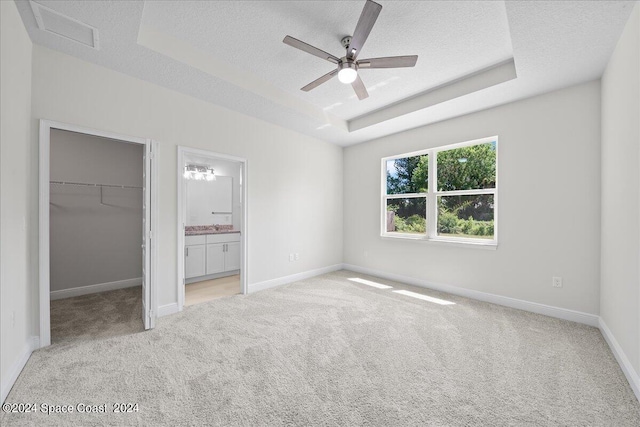 unfurnished bedroom featuring a spacious closet, light carpet, a textured ceiling, and a raised ceiling