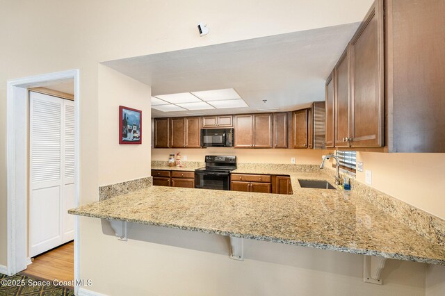 kitchen with light stone countertops, a peninsula, a kitchen breakfast bar, black appliances, and a sink