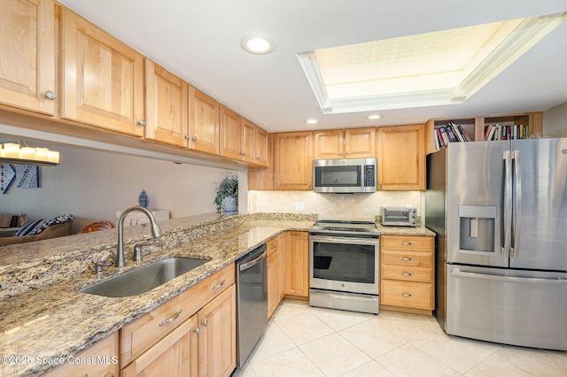 kitchen featuring a tray ceiling, light stone counters, light tile patterned flooring, stainless steel appliances, and a sink