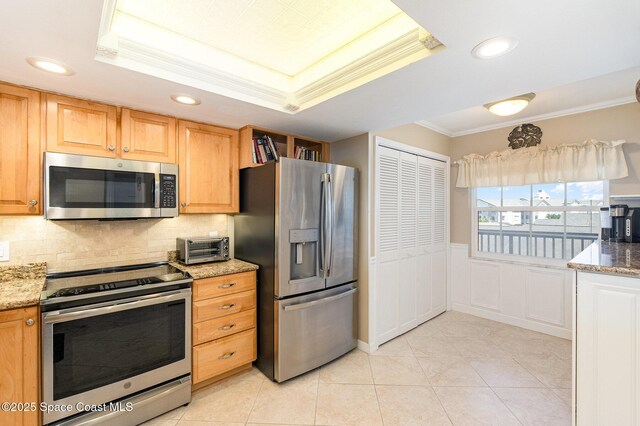 kitchen featuring appliances with stainless steel finishes, light stone countertops, a tray ceiling, and ornamental molding