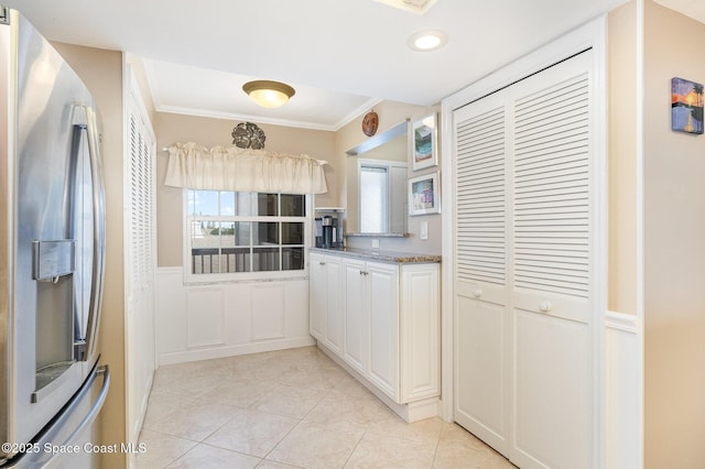 kitchen featuring stainless steel refrigerator with ice dispenser, light tile patterned flooring, wainscoting, crown molding, and light stone countertops