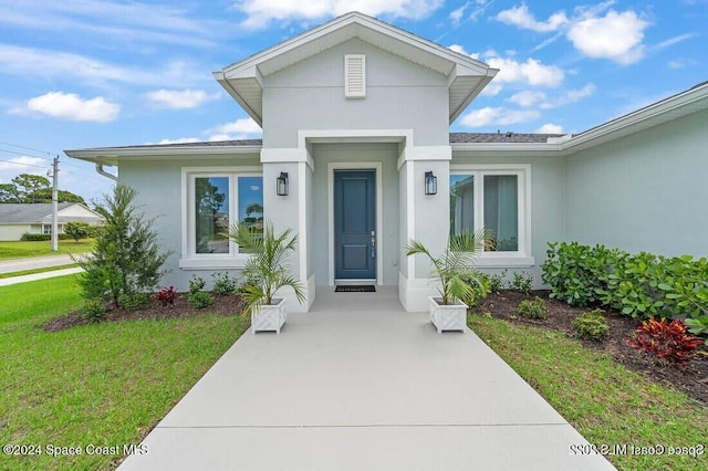 doorway to property with stucco siding, a yard, and roof with shingles