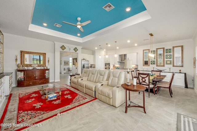 living area with visible vents, a ceiling fan, crown molding, and a tray ceiling