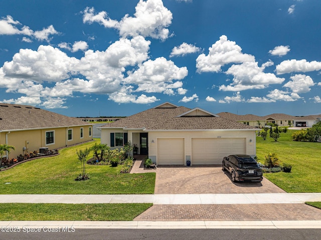 single story home with decorative driveway, roof with shingles, a front yard, a garage, and central AC unit