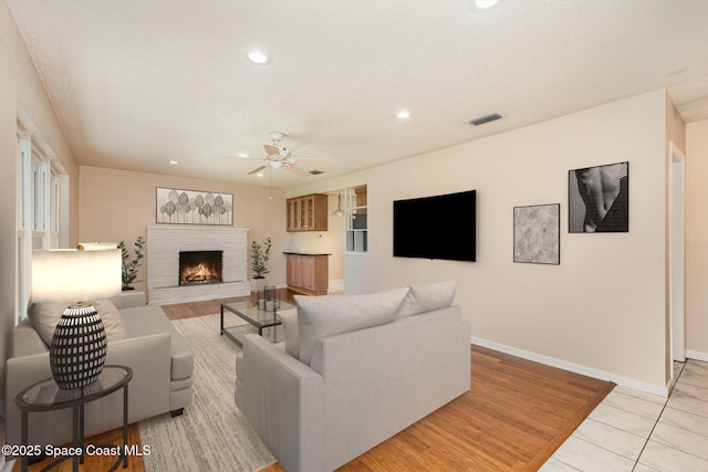 living area featuring visible vents, a textured ceiling, a fireplace, baseboards, and ceiling fan