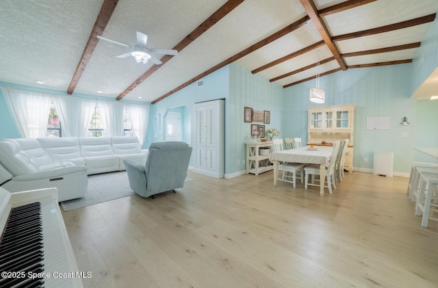 living area with baseboards, ceiling fan, lofted ceiling with beams, light wood-style flooring, and a textured ceiling