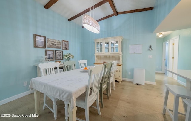 dining room with beam ceiling, light wood finished floors, high vaulted ceiling, and baseboards