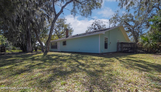 rear view of house with a lawn, a chimney, and fence