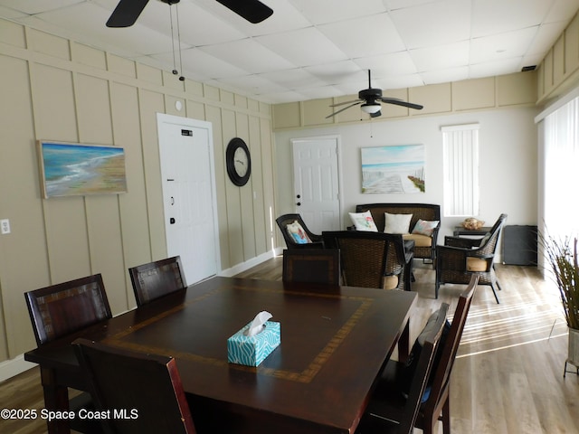 dining room with a decorative wall, wood finished floors, a drop ceiling, and ceiling fan