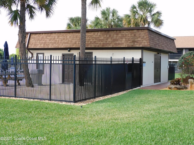 exterior space with a front lawn, fence, roof with shingles, stucco siding, and mansard roof