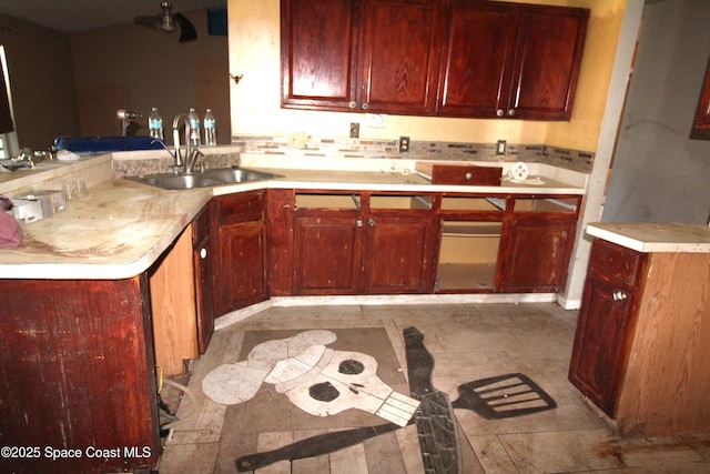 kitchen with a sink, backsplash, a peninsula, light countertops, and dark brown cabinets