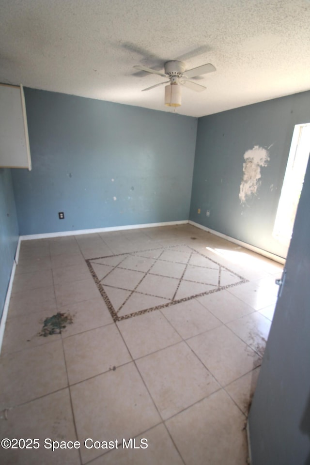 tiled spare room featuring baseboards, a textured ceiling, and ceiling fan