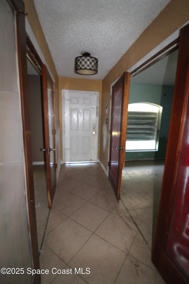 corridor featuring baseboards, a textured ceiling, and light tile patterned flooring