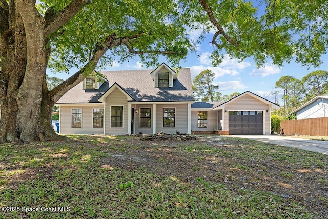 cape cod home featuring a shingled roof, concrete driveway, a garage, and fence