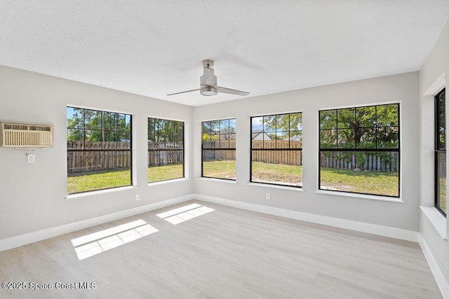 unfurnished sunroom featuring a wall mounted air conditioner, a healthy amount of sunlight, and ceiling fan