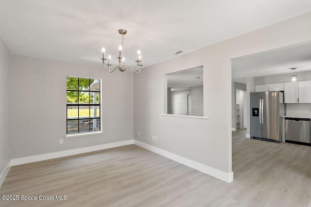 spare room with light wood finished floors, visible vents, baseboards, and an inviting chandelier