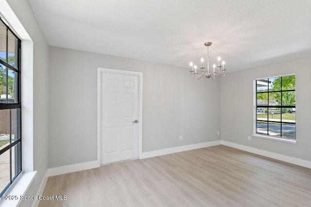 empty room featuring light wood-type flooring, baseboards, and a chandelier