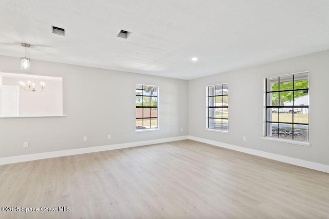 empty room with a chandelier, light wood-type flooring, and baseboards