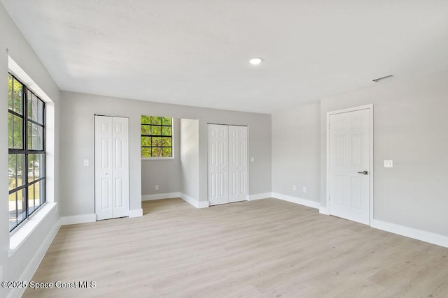 unfurnished bedroom with multiple windows, light wood-type flooring, and multiple closets