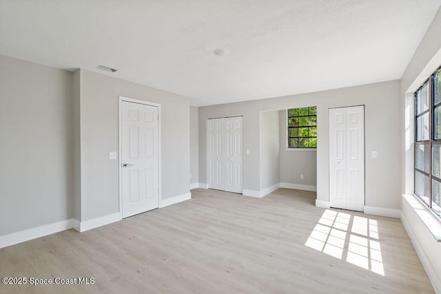 unfurnished bedroom with light wood finished floors, baseboards, and two closets