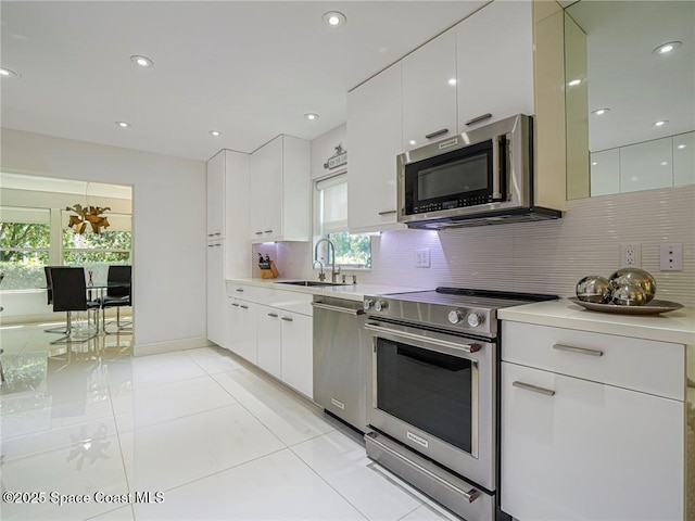 kitchen with modern cabinets, a sink, backsplash, appliances with stainless steel finishes, and light countertops