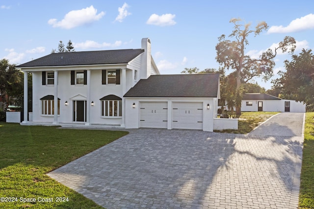 greek revival house featuring stucco siding, a front lawn, decorative driveway, an attached garage, and a chimney