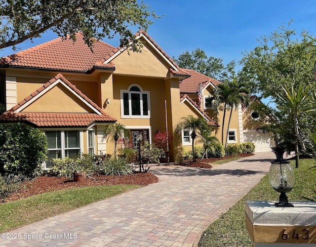 mediterranean / spanish house with stucco siding, a tiled roof, and decorative driveway