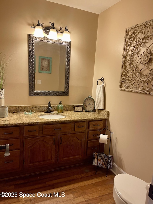 half bathroom featuring toilet, vanity, baseboards, and wood finished floors