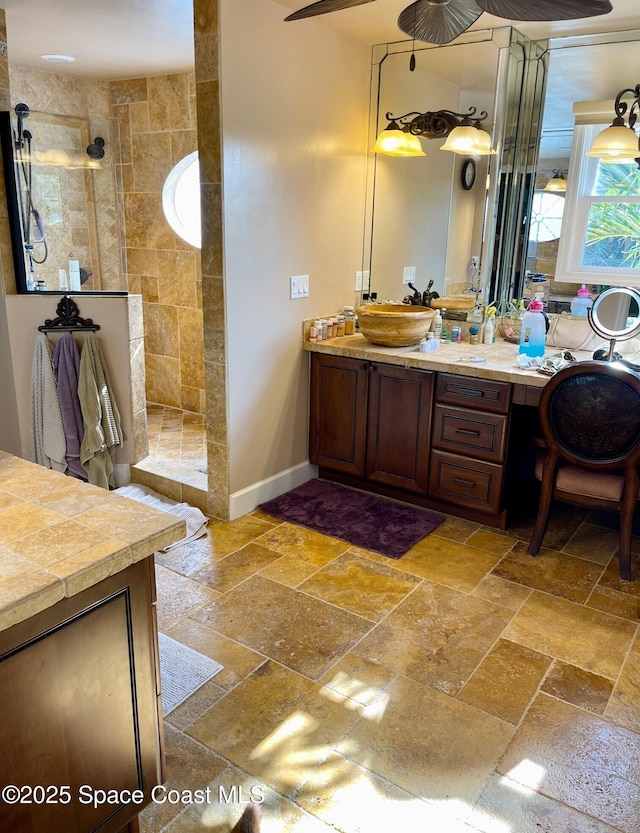 bathroom featuring baseboards, stone tile floors, vanity, and a walk in shower