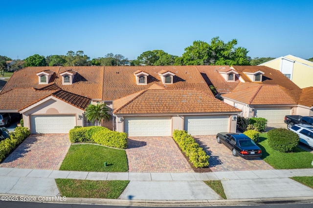 view of front facade with stucco siding, an attached garage, a tile roof, and decorative driveway