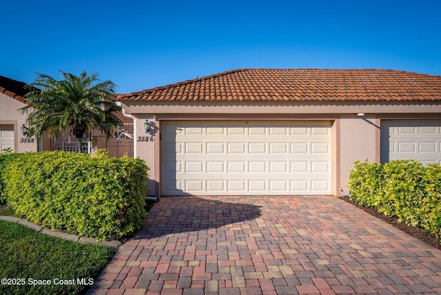 single story home with stucco siding, a tile roof, decorative driveway, and a garage