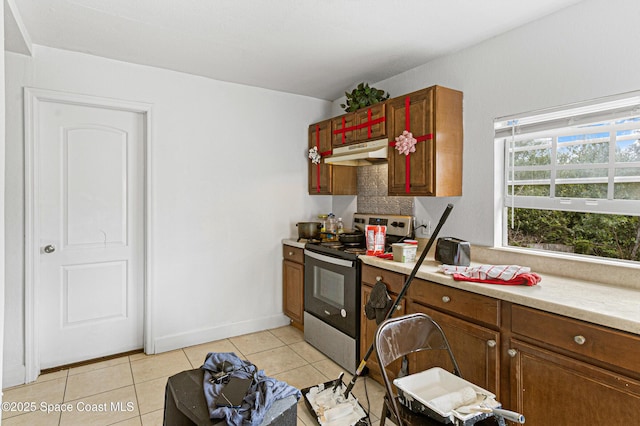 kitchen featuring under cabinet range hood, light countertops, light tile patterned floors, electric stove, and brown cabinetry