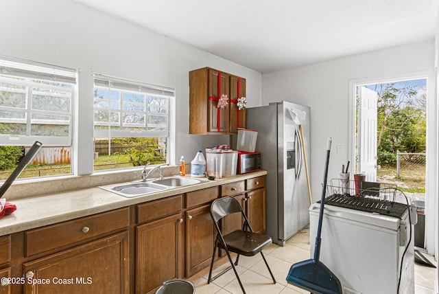 kitchen featuring brown cabinets, a sink, light tile patterned flooring, stainless steel fridge with ice dispenser, and light countertops