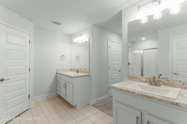 bathroom featuring a shower stall, two vanities, visible vents, and a sink