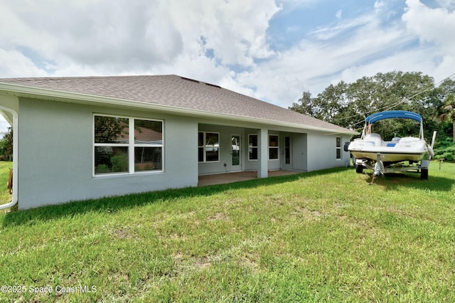 back of property with a patio area, a lawn, a shingled roof, and stucco siding