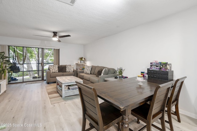 dining room featuring baseboards, a ceiling fan, light wood-type flooring, and a textured ceiling