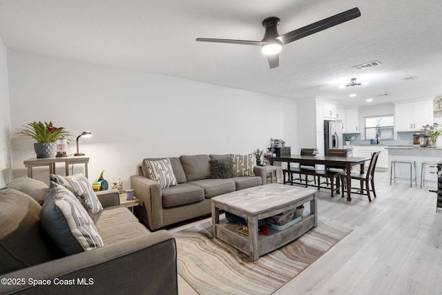 living area featuring visible vents, a textured ceiling, light wood-style flooring, and a ceiling fan