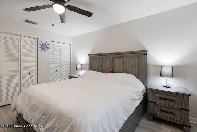 bedroom featuring visible vents, multiple closets, light wood-style floors, and a ceiling fan