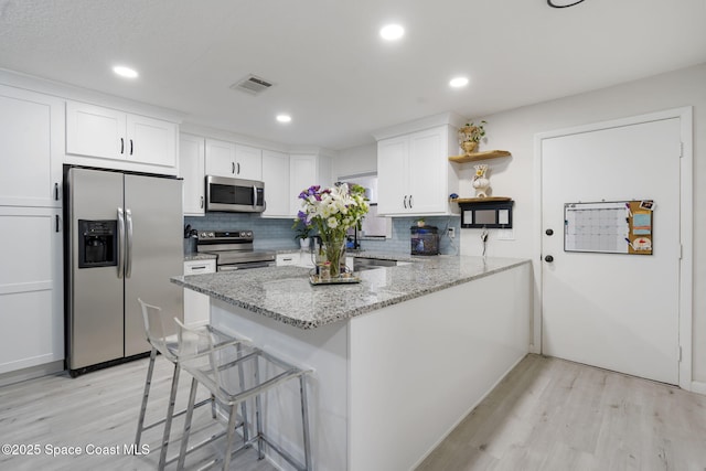 kitchen with visible vents, open shelves, white cabinetry, stainless steel appliances, and a peninsula