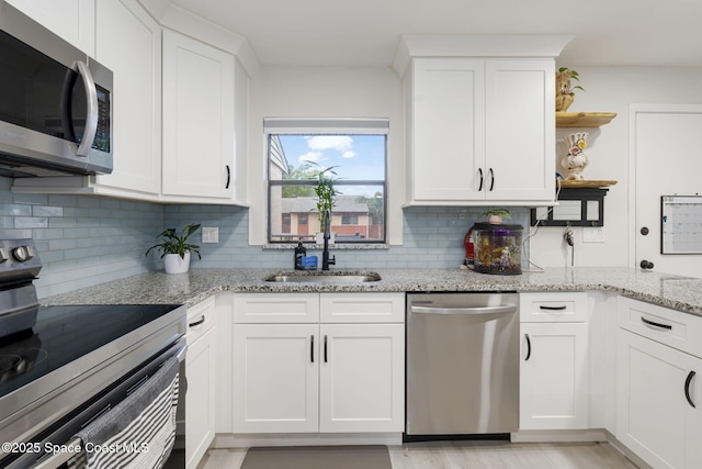 kitchen with open shelves, a sink, backsplash, stainless steel appliances, and white cabinets