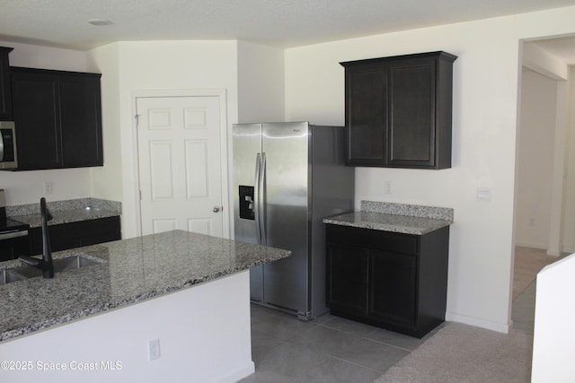 kitchen featuring a sink, appliances with stainless steel finishes, light tile patterned flooring, light stone countertops, and dark cabinets