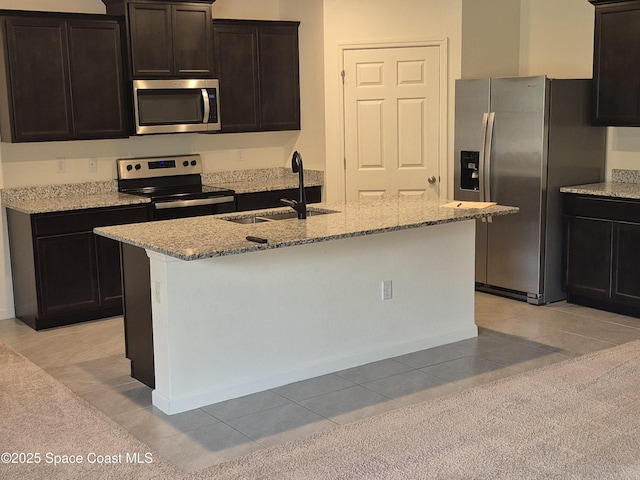 kitchen featuring light stone counters, a center island with sink, appliances with stainless steel finishes, and a sink